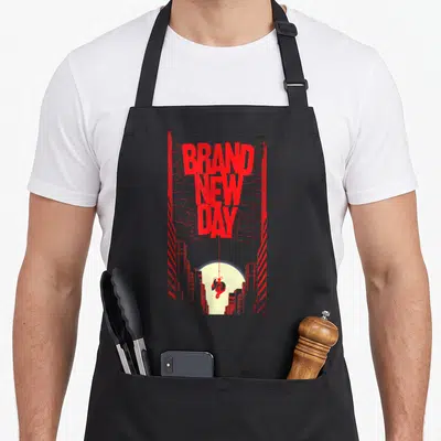 Tablier de cuisine noir avec l'inscription Brand New Day en rouge et un personnage suspendu à une toile entre des tours.