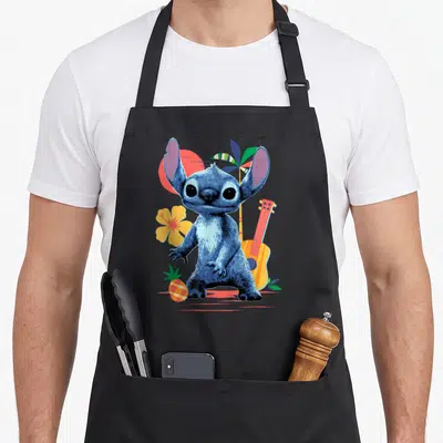 Tablier de cuisine noir avec Stitch, hibiscus jaune, ukulélé orange et ananas stylisé sur fond tropical.
