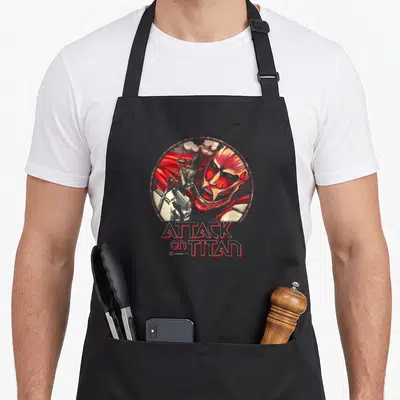 Tablier de cuisine noir avec illustration circulaire d'Eren Yeager affrontant le Titan Colossal et le titre Attack on Titan en rouge.