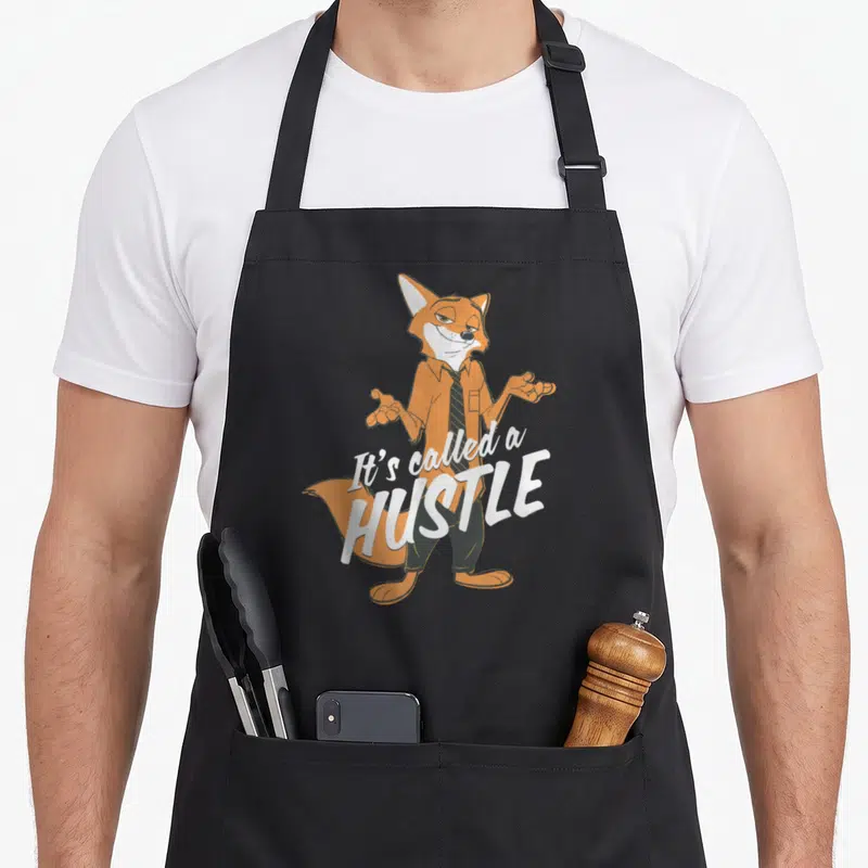 Tablier de cuisine noir avec l'illustration du renard Nick Wilde et le texte It's Called a Hustle en blanc.
