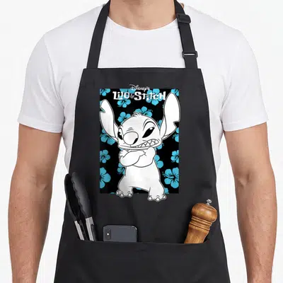 Tablier de cuisine noir avec Stitch aux bras croisés et des fleurs de hibiscus bleues en arrière-plan.