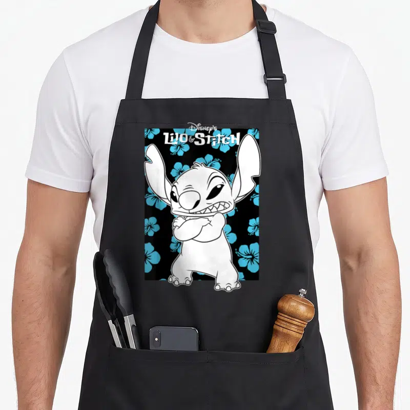 Tablier de cuisine noir avec Stitch aux bras croisés et des fleurs de hibiscus bleues en arrière-plan.