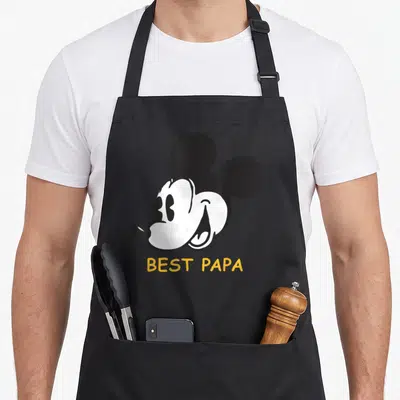 Tablier de cuisine noir avec tête de Mickey souriante et inscription jaune Best Papa en dessous.