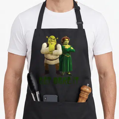 Tablier de cuisine noir avec Shrek, Fiona et l'inscription verte Get Ogre It en bas.
