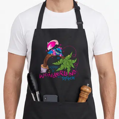 Tablier de cuisine noir avec Stitch en Chat du Cheshire sur une branche de palmier rose et verte.