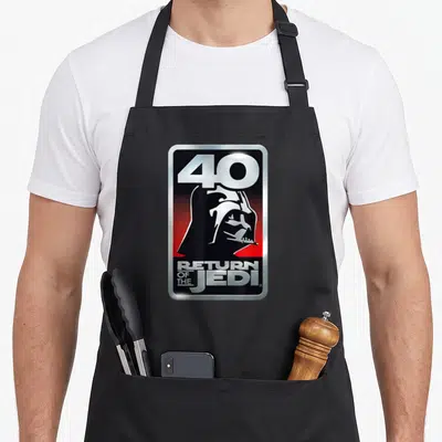 Tablier de cuisine noir avec un logo 40 Return of the Jedi et le profil de Vader en argent sur fond rouge et noir.
