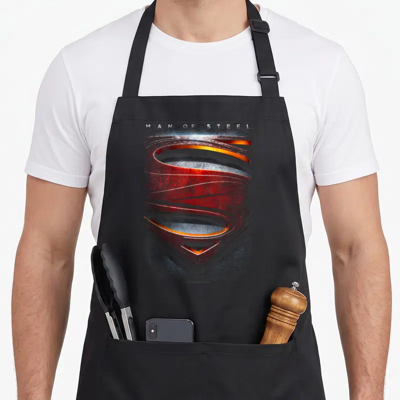 Tablier de cuisine noir avec un grand blason stylisé rouge et argenté portant l'inscription Man of Steel en haut.