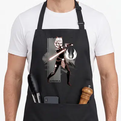 Tablier de cuisine noir avec illustration d'Ahsoka Tano brandissant un sabre laser rose devant un emblème blanc.