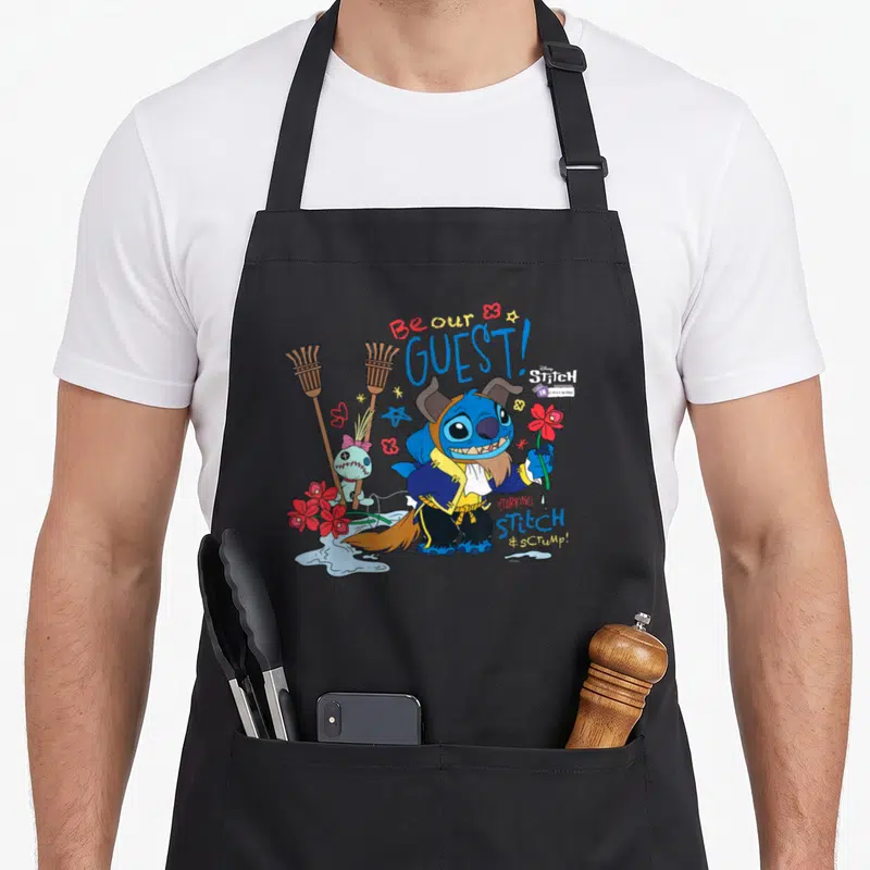 Tablier de cuisine noir avec Stitch déguisé en la Bête tenant une fleur rouge et le texte Be our GUEST.