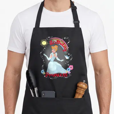Tablier de cuisine noir avec une princesse en robe bleue, un arc-en-ciel et l'inscription anniversaire Princess entourée d'étoiles.