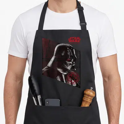 Tablier de cuisine noir avec illustration Darth Vader Rogue One et logo Empire en rouge sur fond sombre géométrique.