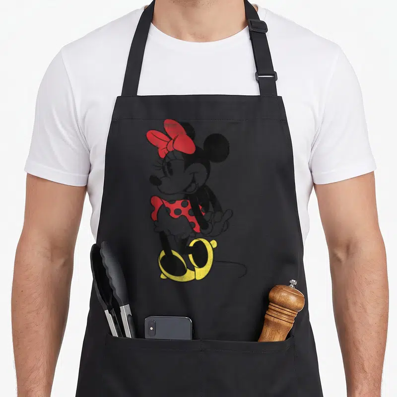 Tablier de cuisine noir avec illustration vintage de Minnie Mouse aux couleurs rouges et jaunes sur fond uni.
