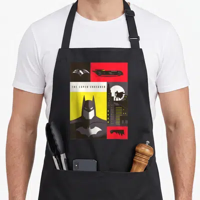Tablier de cuisine noir avec illustration graphique de Batman The Caped Crusader, Bat-symbol et Batmobile sur fond jaune et rouge.