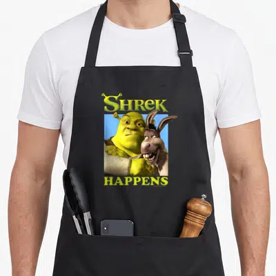 Tablier de cuisine noir avec Shrek et Donkey illustrés sous le texte Shrek Happens en lettres vertes.