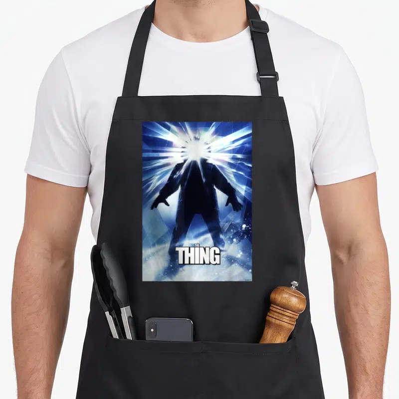 Tablier de cuisine noir avec silhouette rayonnante et texte The Thing en blanc sur fond bleu géométrique.