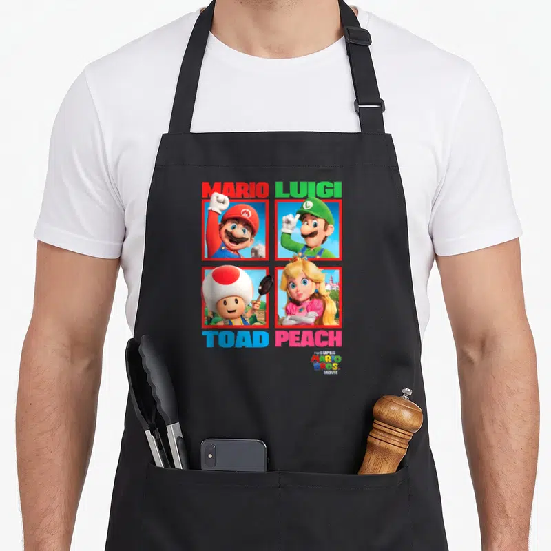 Tablier de cuisine noir avec les portraits de Mario Luigi Toad et Peach disposés en grille colorée sur fond uni.