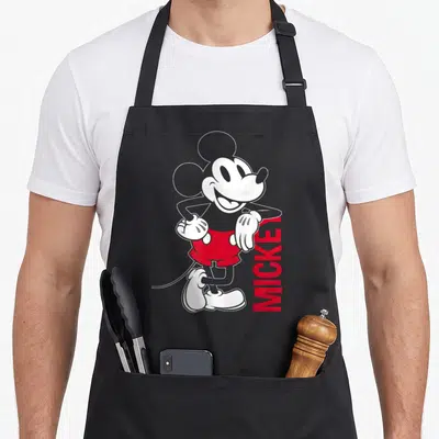 Tablier de cuisine noir avec illustration Mickey Mouse vintage en outline blanc et rouge, texte MICKEY vertical.
