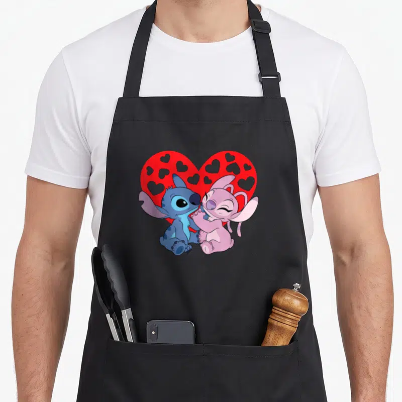 Tablier de cuisine noir avec Stitch bleu et Angel rose s'enlaçant devant un cœur rouge à motifs de cœurs gris.