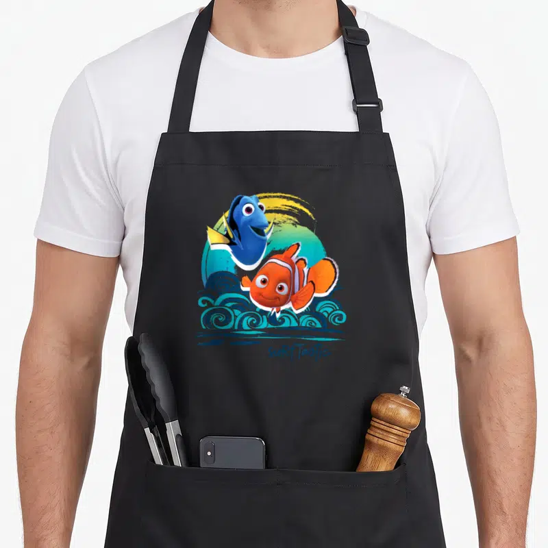 Tablier de cuisine noir avec Nemo, Dory et le texte Surf Tastic sur fond d'ondes stylisées.