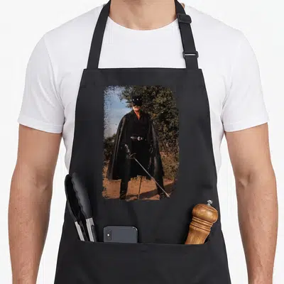 Tablier de cuisine noir avec illustration vintage de Zorro tenant un sabre dans un décor naturel.