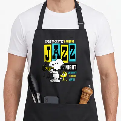 Tablier de cuisine noir avec Snoopy jouant de la trompette et l'inscription JAZZ NIGHT en couleurs vives.