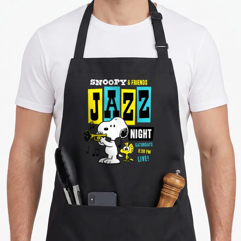 Tablier de cuisine noir avec Snoopy jouant de la trompette et l'inscription JAZZ NIGHT en couleurs vives.