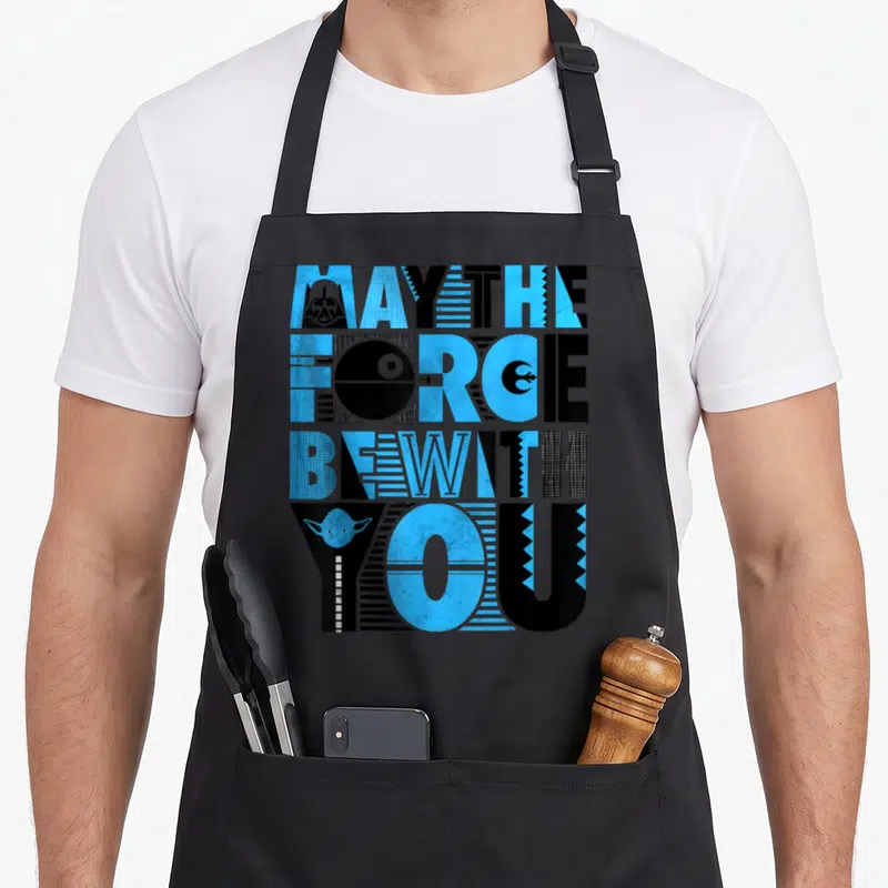Tablier de cuisine noir avec typographie May The Force Be With You bleue et noire intégrant des icônes Star Wars comme Yoda et Darth Vader.