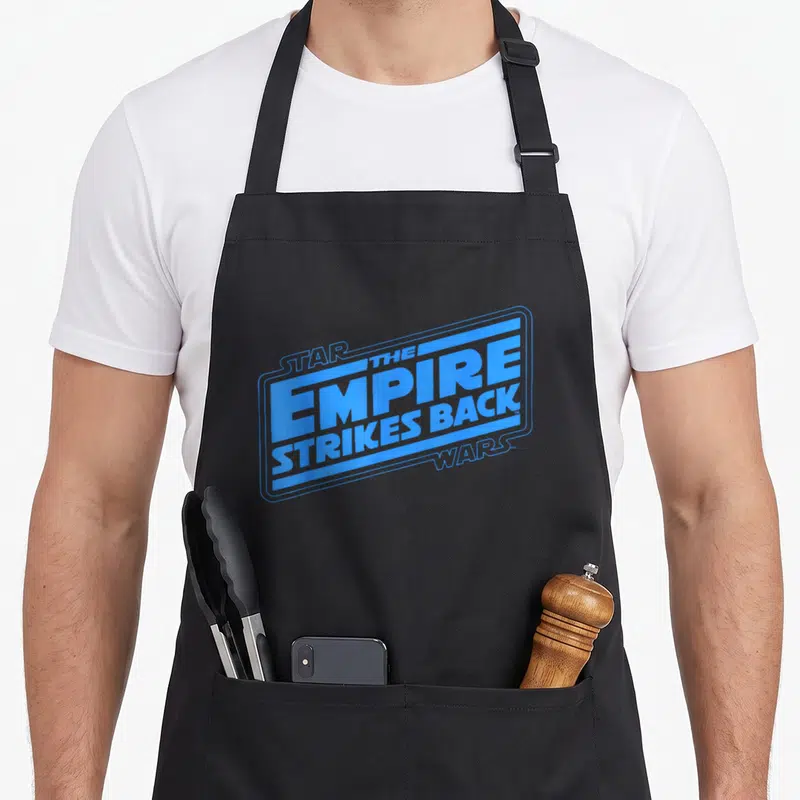 Tablier de cuisine noir avec le logo L'Empire contre-attaque imprimé en bleu vif au centre.