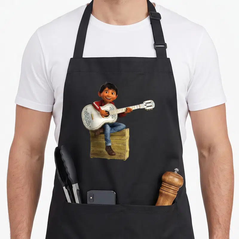 Tablier de cuisine noir avec Miguel Rivera assis sur une caisse jouant d'une guitare blanche ornée de motifs floraux.