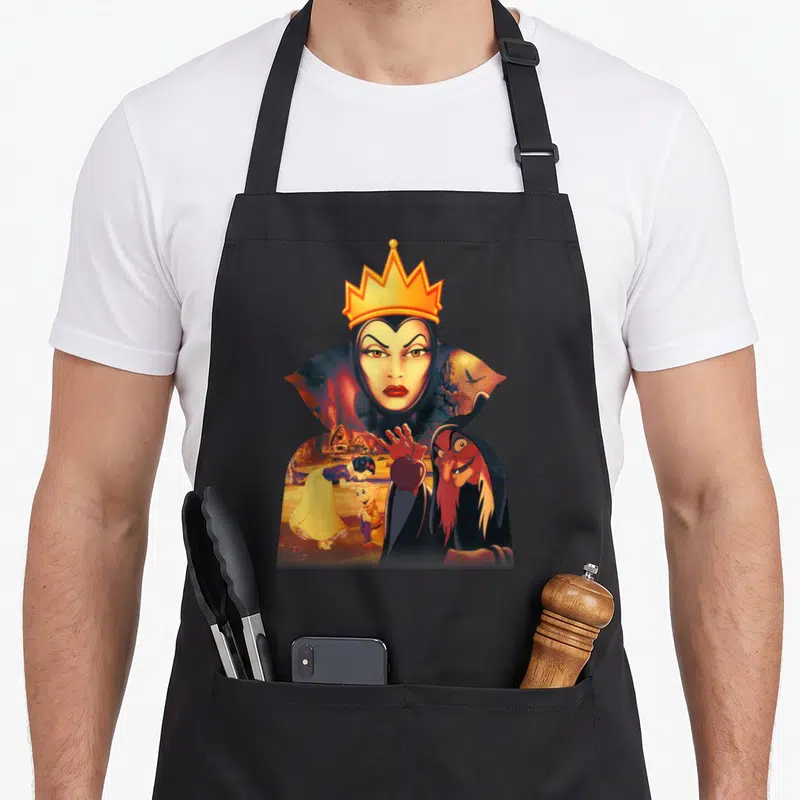 Tablier de cuisine noir avec une illustration de la Reine Maléfique tenant un pommeau rouge devant un village.