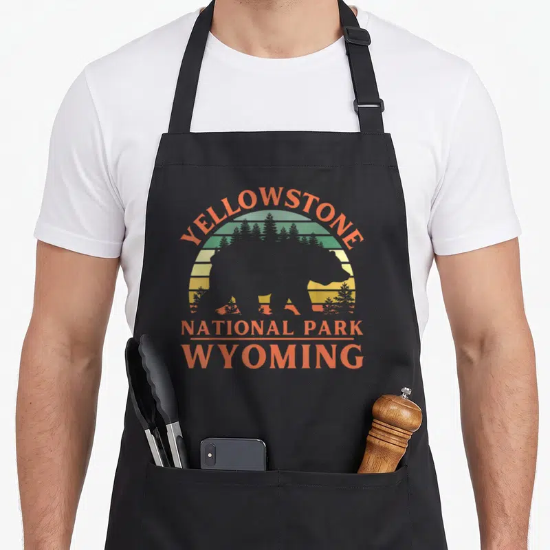 Tablier de cuisine noir avec silhouette d'ours et texte Yellowstone National Park Wyoming en orange et vert.