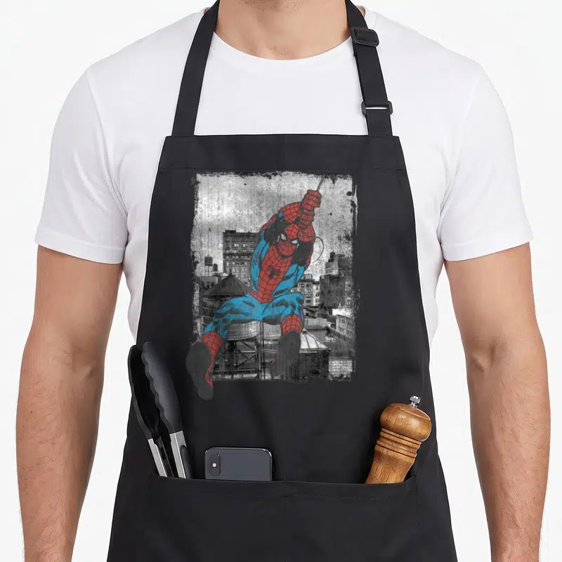 Tablier de cuisine noir avec une illustration vintage de Spider-Man en tenue rouge et bleue se balançant au-dessus d'une ville en gris.