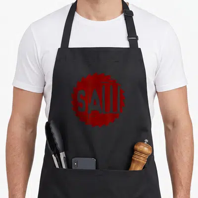 Tablier de cuisine noir avec un logo circulaire rouge représentant une lame de scie et le texte SAW en blanc.