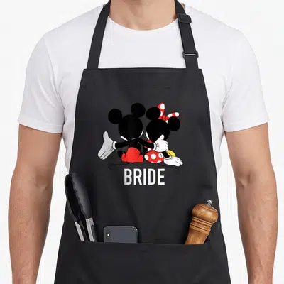 Tablier de cuisine noir avec une illustration de la mariée assise à côté de Mickey et Minnie Mouse.