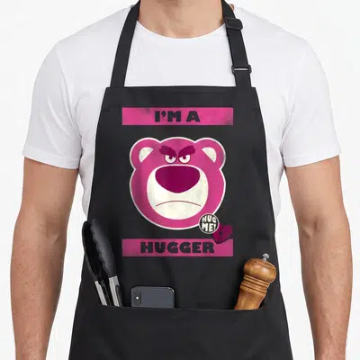 Tablier de cuisine noir avec le visage rose de Lotso et les mots I'M A HUGGER en lettres grises sur fond magenta.