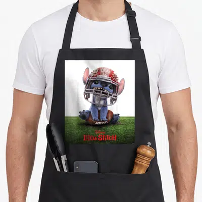 Tablier de cuisine noir avec Stitch portant un casque de football sur un terrain vert.