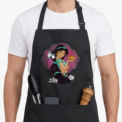 Tablier de cuisine noir avec illustration de la princesse Jasmine tenant une lampe dorée dans un cadre ornemental rose et turquoise.
