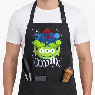 Tablier de cuisine noir avec un alien vert souriant, une fusée rouge et le texte Ooooohh..