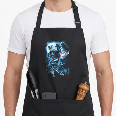 Tablier de cuisine noir avec illustration de Catwoman en position acrobatique sur un fond lunaire bleu et une ville stylisée.