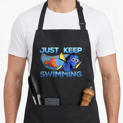 Tablier de cuisine noir avec Dory et Nemo et le texte Just Keep Swimming en bleu.