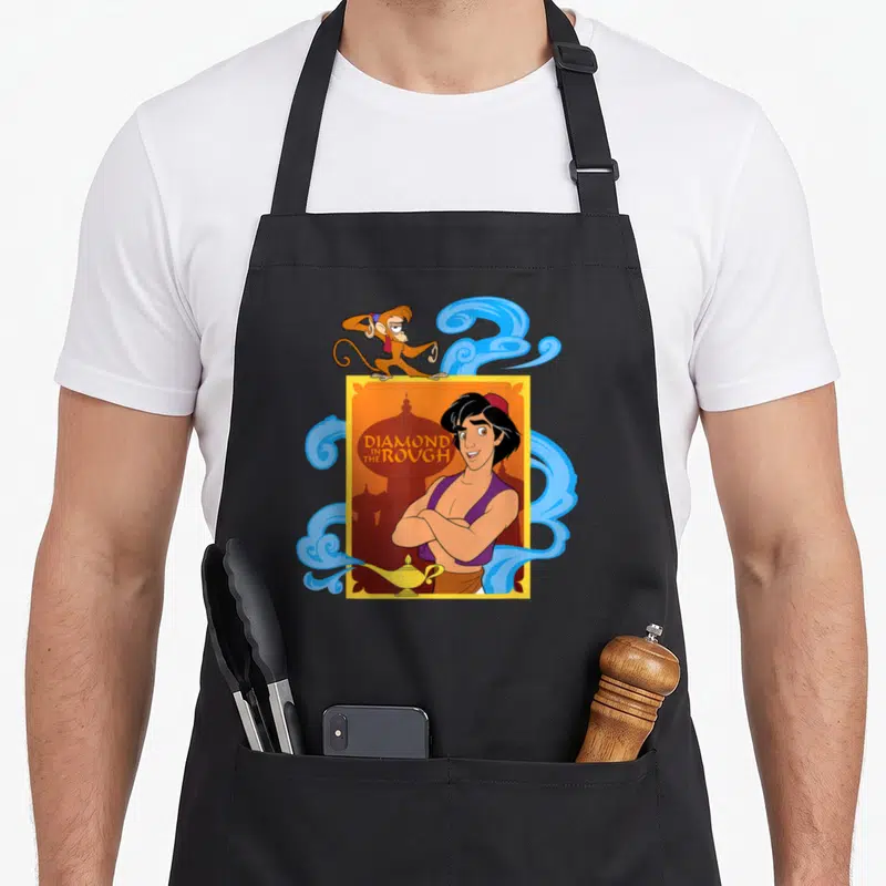 Tablier de cuisine noir avec illustration d'Aladdin Diamond In The Rough, Abu et une lampe dorée.