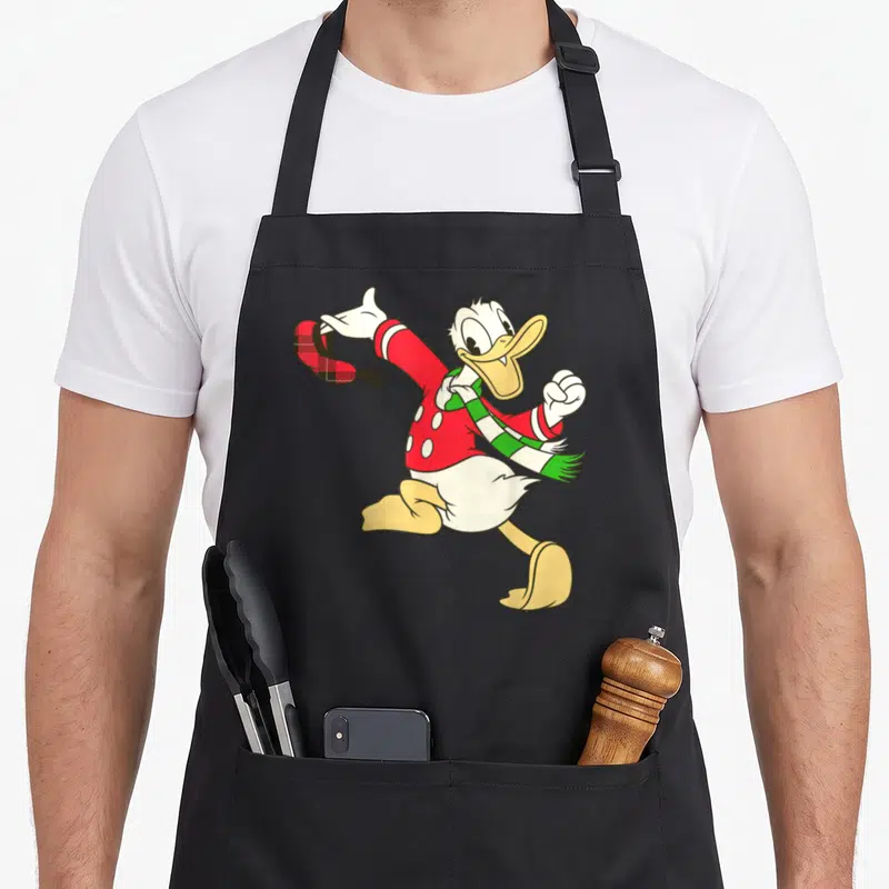 Tablier de cuisine noir avec illustration colorée de Donald Duck portant un foulard vert et tenant un chapeau à carreaux rouges.