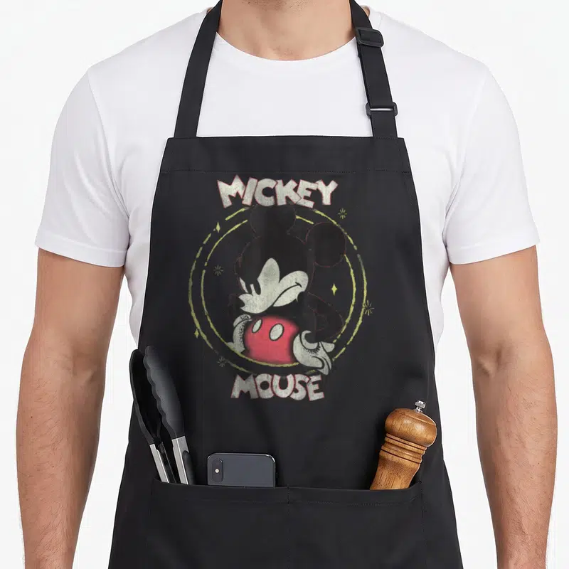 Tablier de cuisine noir avec portrait stylisé de Mickey Mouse et texte Mickey Mouse en lettres blanches.