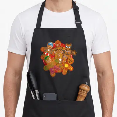 Tablier de cuisine noir avec des Avengers en biscuits de Noël colorés sur une assiette rouge.