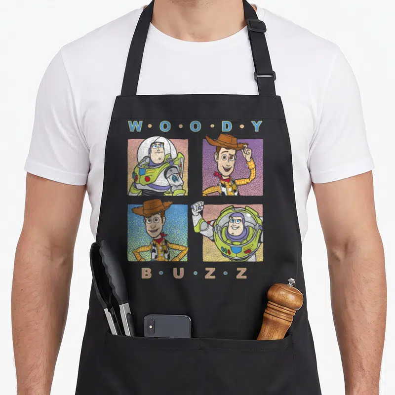 Tablier de cuisine noir avec illustration de Woody et Buzz Lightyear en quatre carrés colorés et texte stylisé.