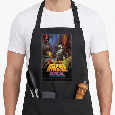 Tablier de cuisine noir avec illustration de Yoda sur Dagobah et le titre The Empire Strikes Back en lettres colorées.