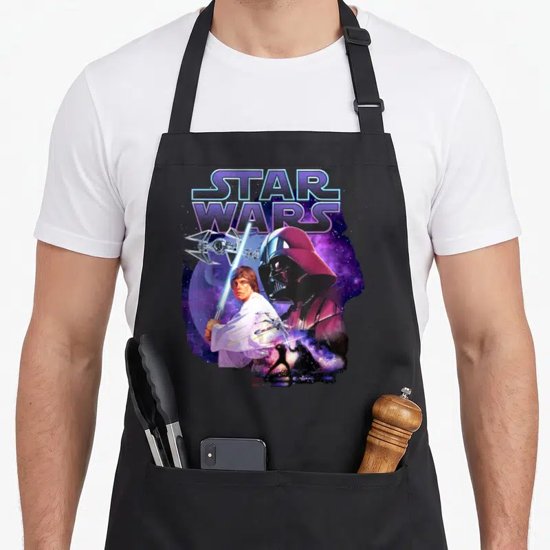 Tablier de cuisine noir avec illustration Luke Skywalker, Dark Vador et vaisseaux stellaires sur fond violet.