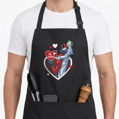 Tablier de cuisine noir avec Harley Quinn et le Joker s'enlaçant autour d'un cœur rouge portant l'inscription My Puddin'.