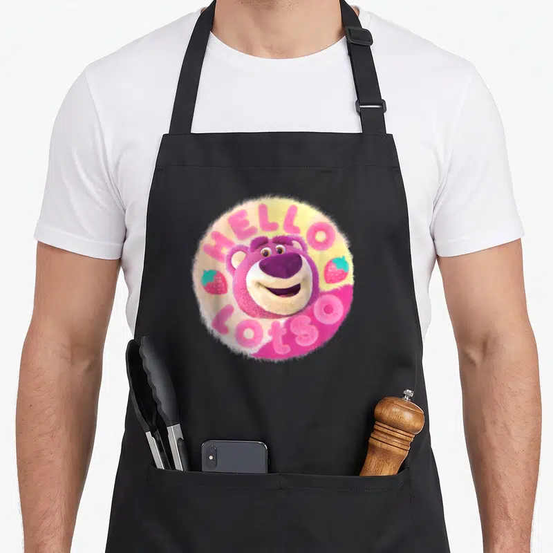 Tablier de cuisine noir avec un ours rose féroce et des fraises dans un motif circulaire.
