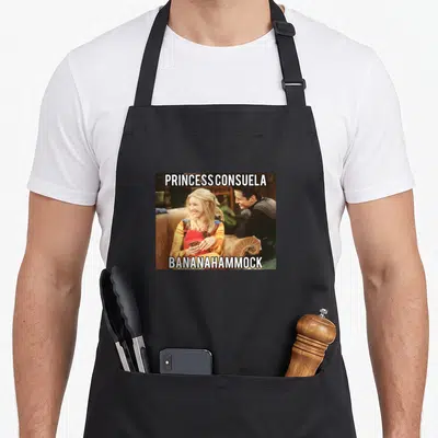 Tablier de cuisine noir avec une illustration de Phoebe Buffay et le texte Princess Consuela Bananahammock imprimé en blanc.